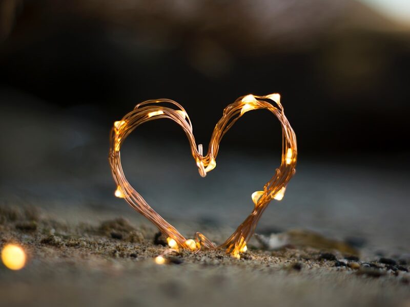 close-up photography of heart shaped fairy lite on brown sand